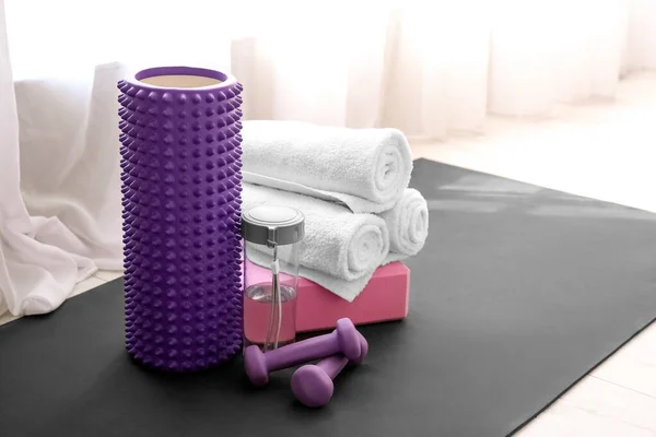 Foam roller, bottle of water, block, dumbbells and towels near window in room