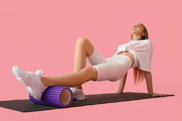 Young woman training with foam roller on pink background