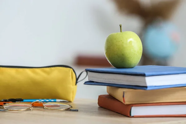 Apple with school books and pencil case on table in classroom