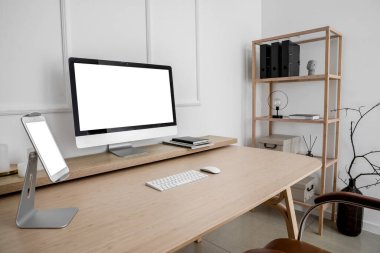Modern workplace with computer and tablet near light wall