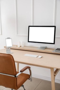 Modern workplace with computer and tablet near light wall