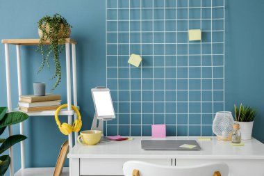 Mavi duvarın yanında dizüstü bilgisayarı ve tablet bilgisayarı olan modern işyeri