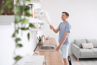 Genç adam mutfakta toz fırçasıyla temizlik yapıyor.