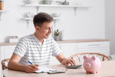 Young man using calculator at table in kitchen