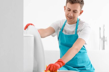 Young man cleaning toilet bowl with rag in bathroom