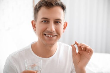 Yatak odasında vitamin takviyesi ve bir bardak su olan genç adam, yakın plan.