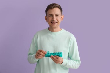 Young man holding container with pills on violet background