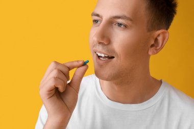 Sarı arka planda vitamin alan genç adam, yakın plan.