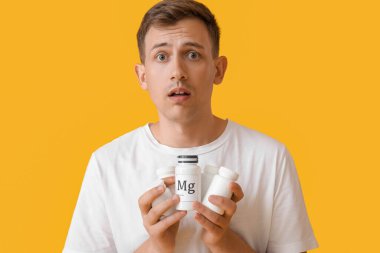 Shocked young man with pill bottles on yellow background