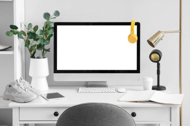 Modern computer and stylish shoes on table near white wall