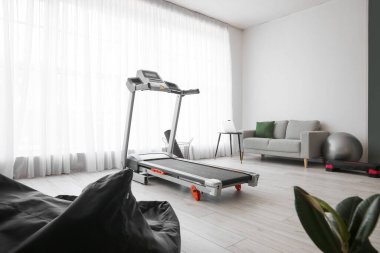 Koşu bandı, kanepe ve spor malzemeleriyle aydınlık oturma odasının içinde.