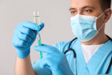 Doctor with ampule and syringe on light background