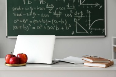Plate with apples, laptop, books and eyeglasses on table in classroom