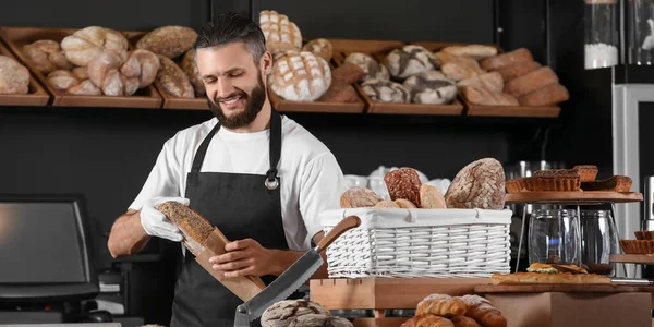 Male baker packaging fresh bread for customer in shop