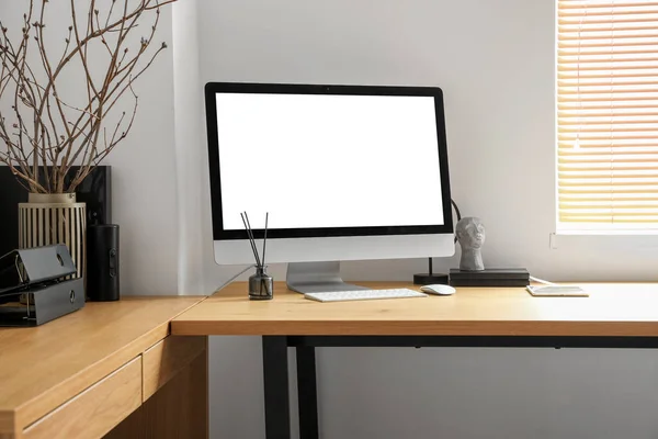 Modern workplace with computer, tablet and tree branches in vase near light wall