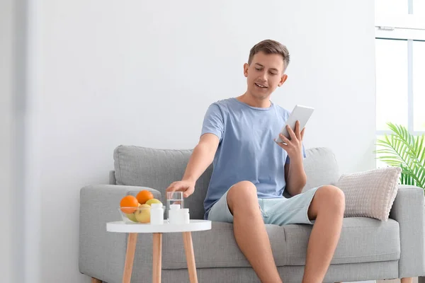 Young man with tablet computer taking vitamin supplement at home