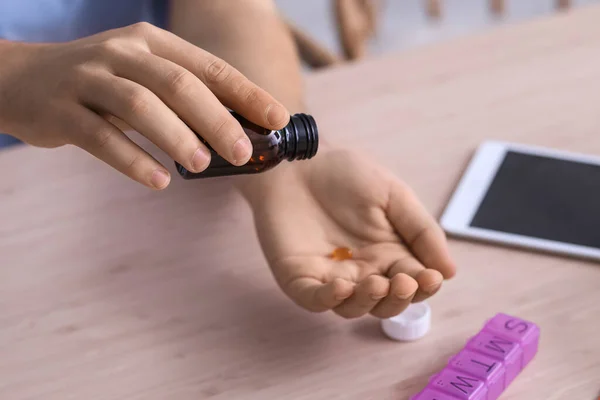 Young man taking vitamin supplement at table in kitchen, closeup