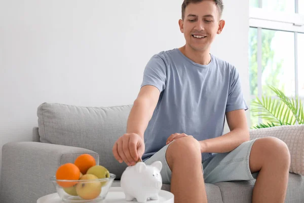 Young Man Putting Coin Piggy Bank Table Home — Stock Photo, Image