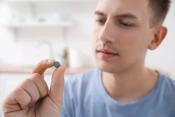 Young man with vitamin supplement at home, closeup