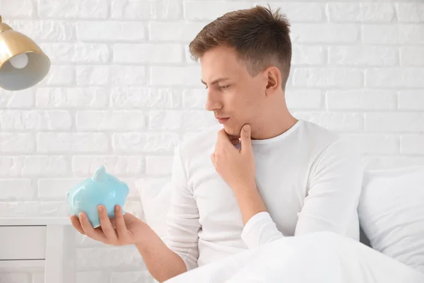 Thoughtful Young Man Piggy Bank Lying Bed — ストック写真