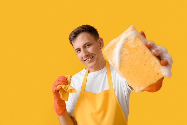 Young man with cleaning sponge and rag on yellow background
