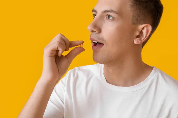 Young man taking vitamin on yellow background