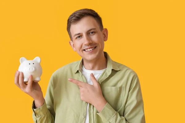 Young Man Pointing White Piggy Bank Yellow Background — Stockfoto