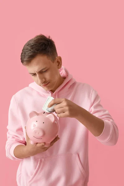 Young Man Putting Money Piggy Bank Pink Background — 图库照片