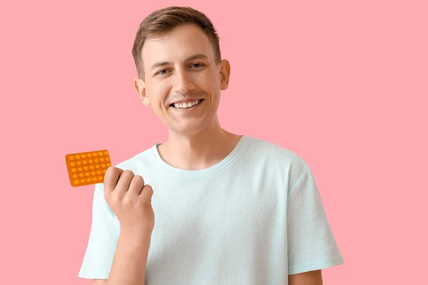 Young man with blister of pills on pink background