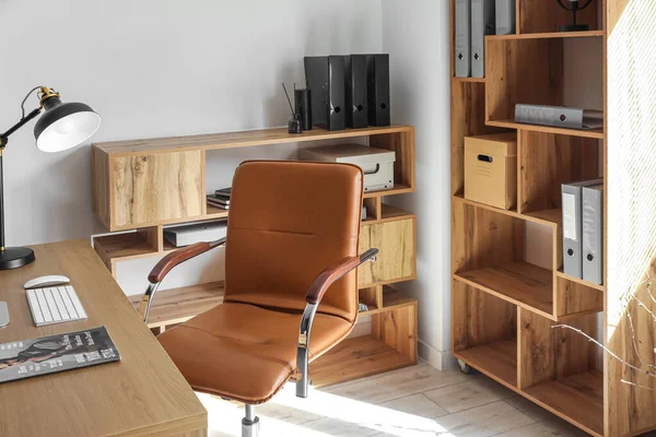 Interior of light office with desk, chair and shelving unit