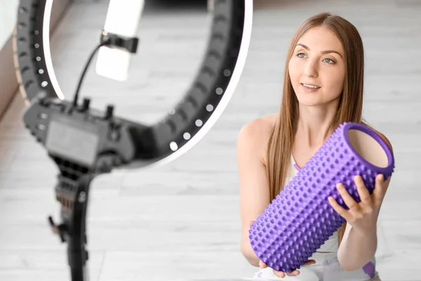 Young woman with foam roller recording video at home