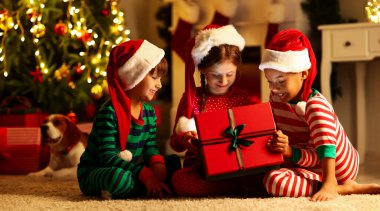 Cute little children in Santa hats opening Christmas gift at home
