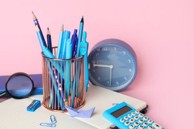 Okul kırtasiyeli bardak ve pembe arka planda çalar saat.