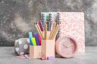 Okul kırtasiyeli fincanlar, kalem kutusu ve Grunge arka planında çalar saat.