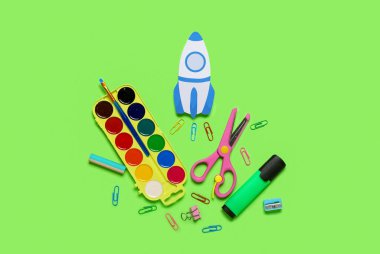 Paper rocket with school stationery on green background