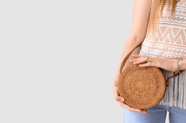 Young woman with stylish rattan bag on light background