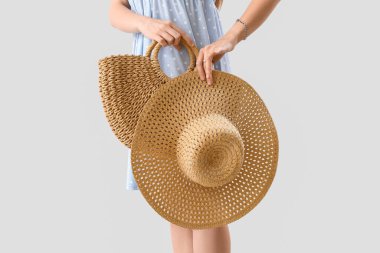 Woman holding rattan handbag and wicker hat on light background