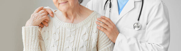 Senior woman with doctor on grey background