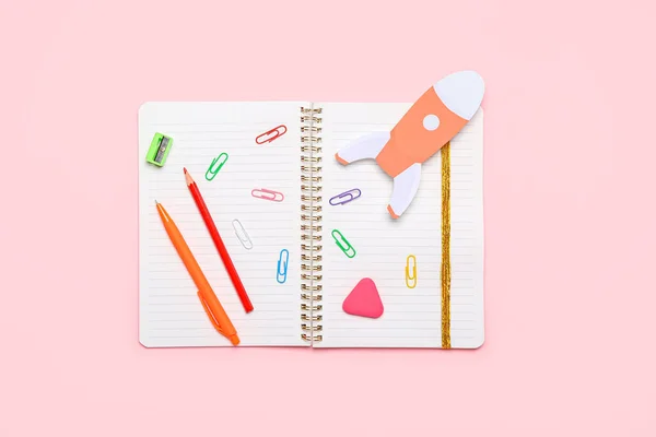 Paper rocket with school stationery on pink background