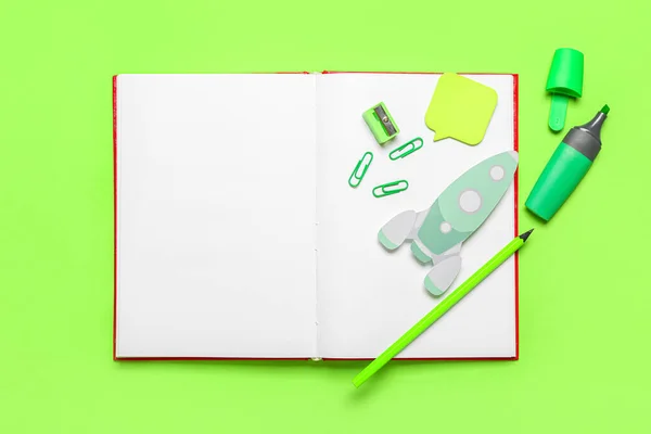 Paper rocket with notebook and school stationery on green background