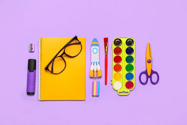 Paper rocket with school stationery and eyeglasses on violet background