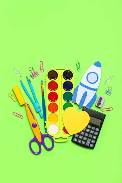 Paper rocket with school stationery on green background