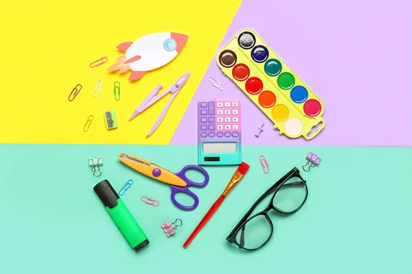 Paper rocket with school stationery and eyeglasses on color background