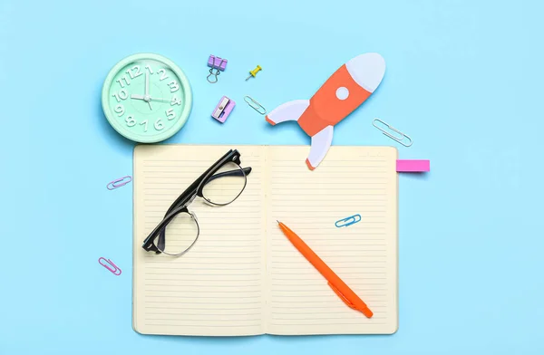 Paper rocket with school stationery and alarm clock on blue background