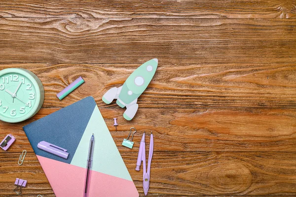 Paper rocket with school stationery and alarm clock on wooden background