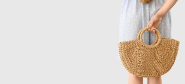 Elegant young woman with rattan bag on light background with space for text, back view