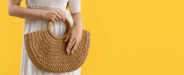 Stylish young woman with rattan bag on yellow background with space for text