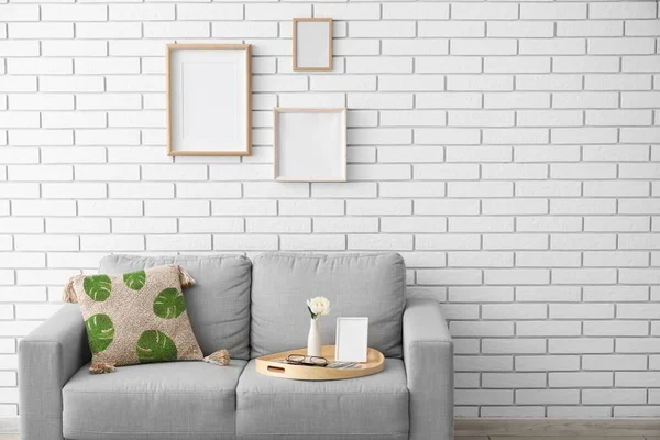 Comfortable sofa near light brick wall with blank photo frames