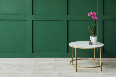 Orkide çiçeği ve sazlık ayırıcı yeşil duvarın yanındaki masada.