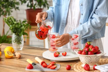 Woman pouring tasty strawberry lemonade into glass on wooden table
